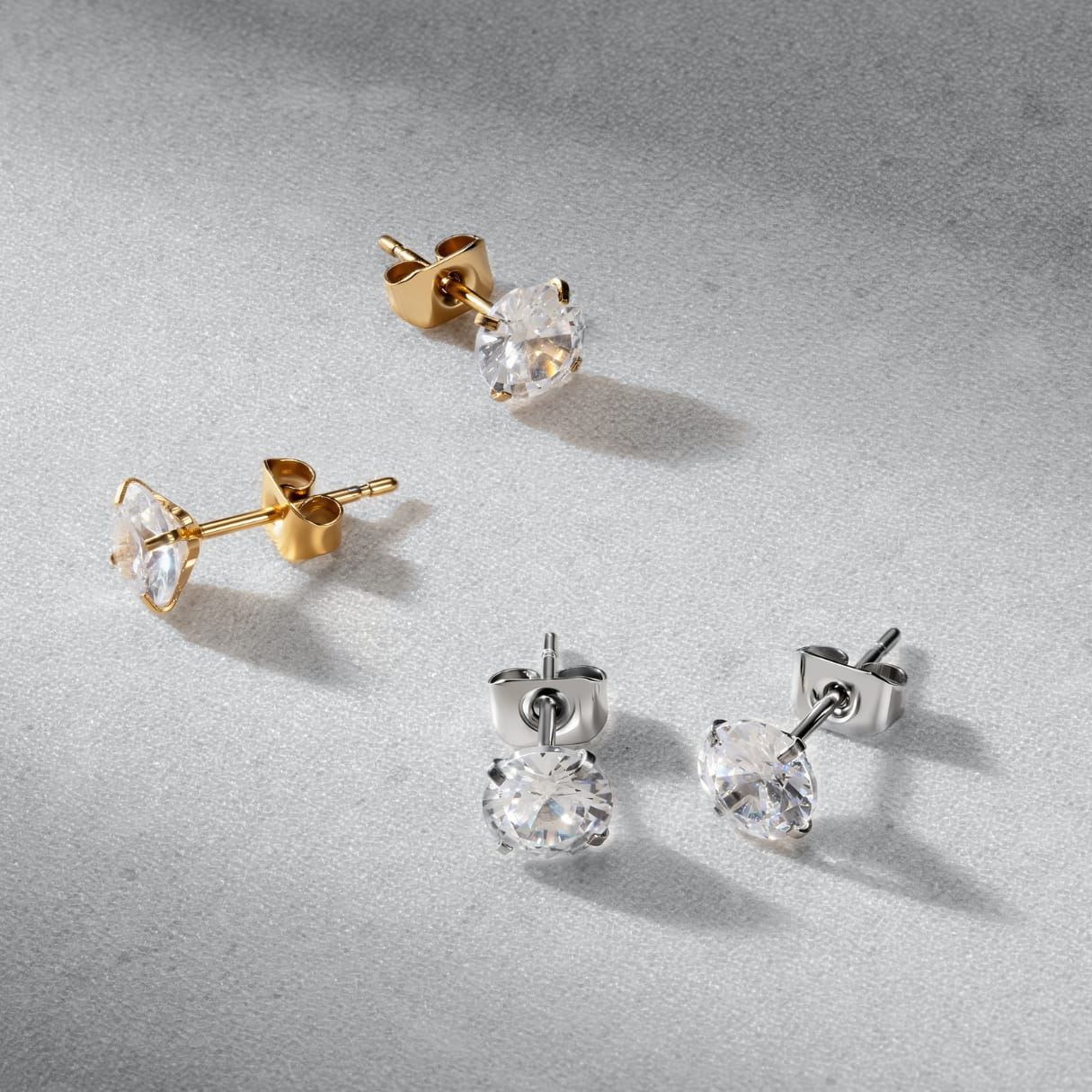 Four pairs of crystal stud earrings in gold, silver on a gray background.