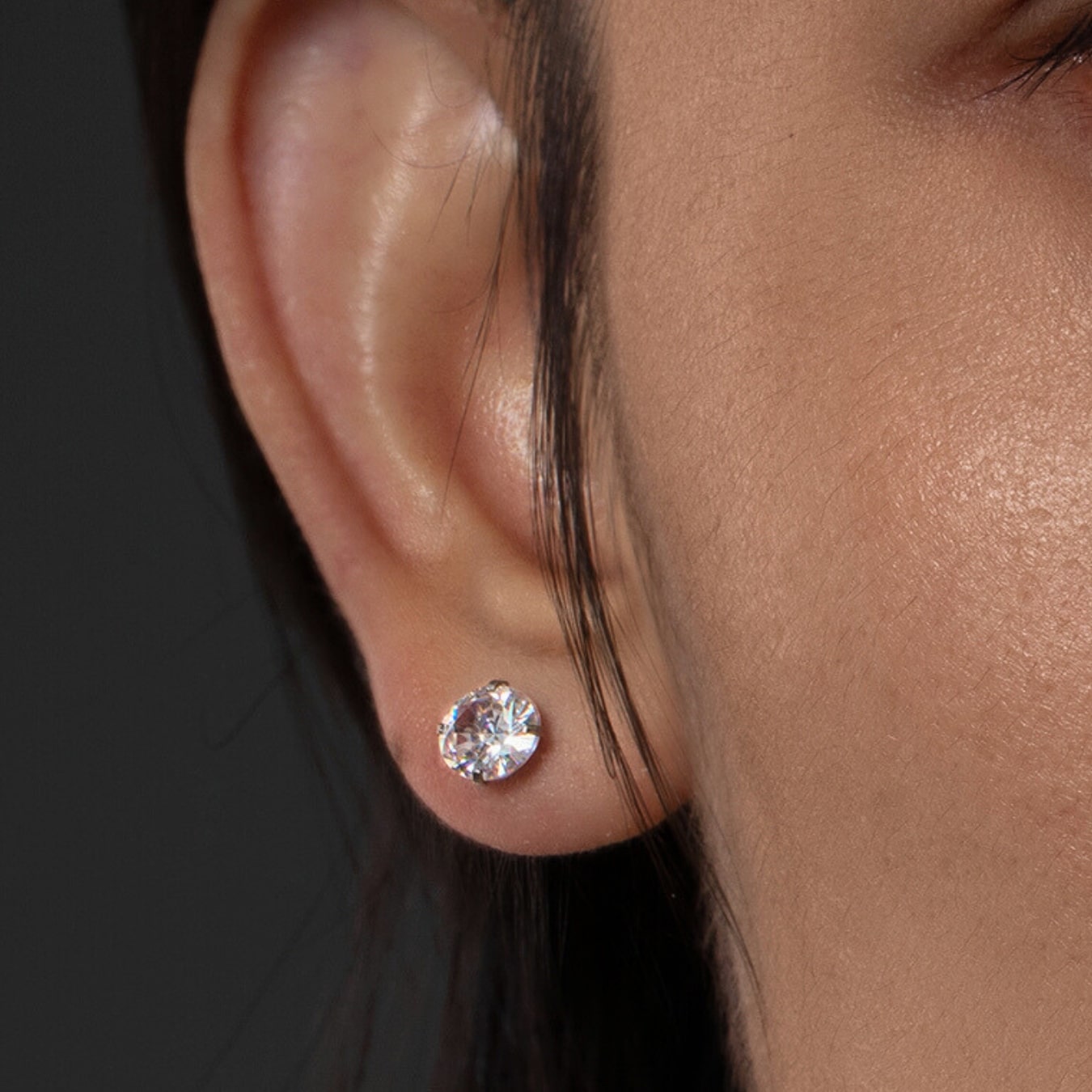 Close-up of an ear wearing a diamond stud earring with a dark background