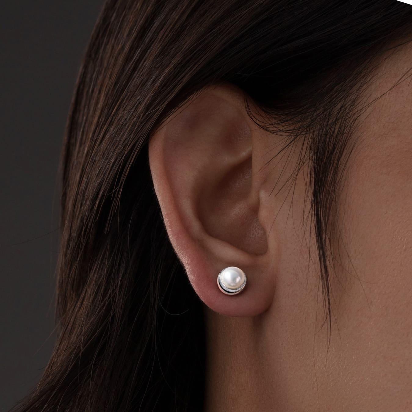 Close-up of an ear wearing a pearl earring with dark hair