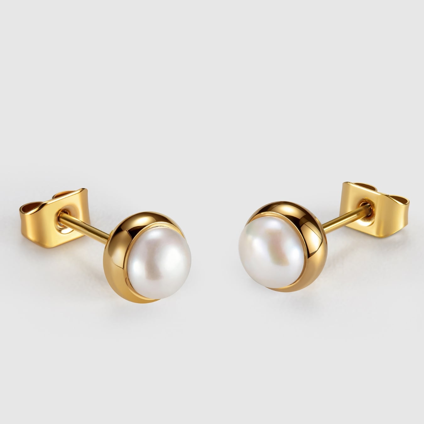 Gold earrings with pearl stones on a light gray background