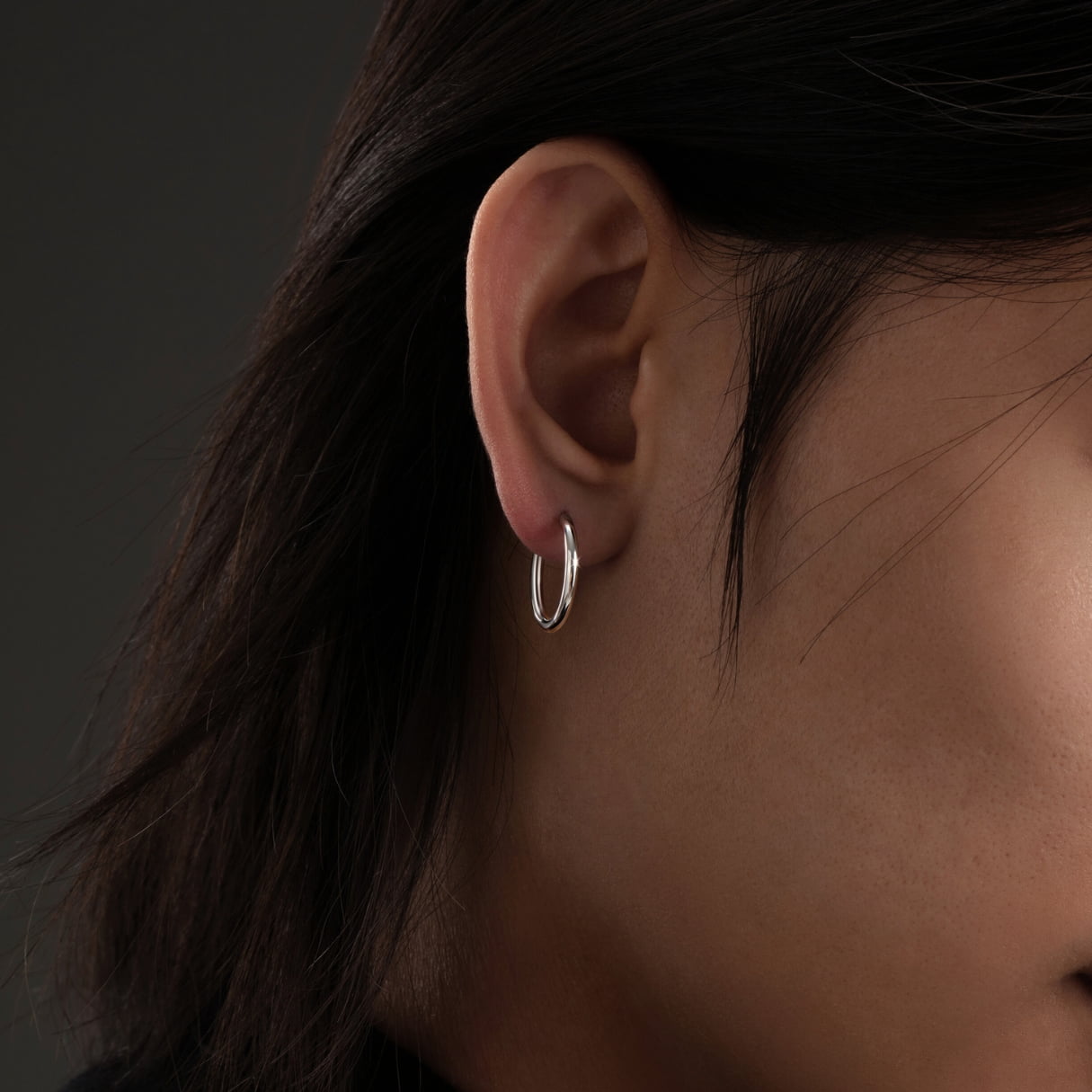 Close-up of an ear wearing a silver hoop earring against a dark background