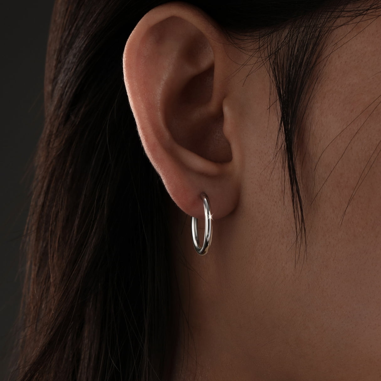 Close-up of an ear wearing a silver hoop earring against a dark background