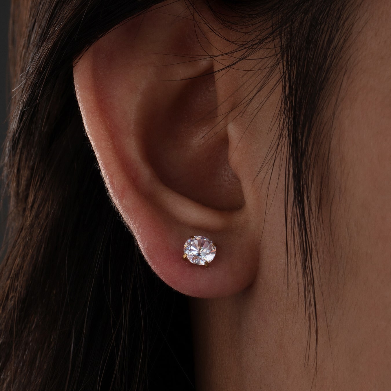 Close-up of an ear wearing a diamond earring with dark hair.