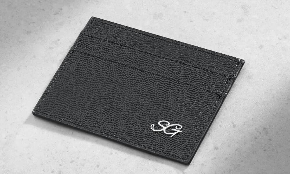 Black textured leather card holder with silver monogram embroidery.