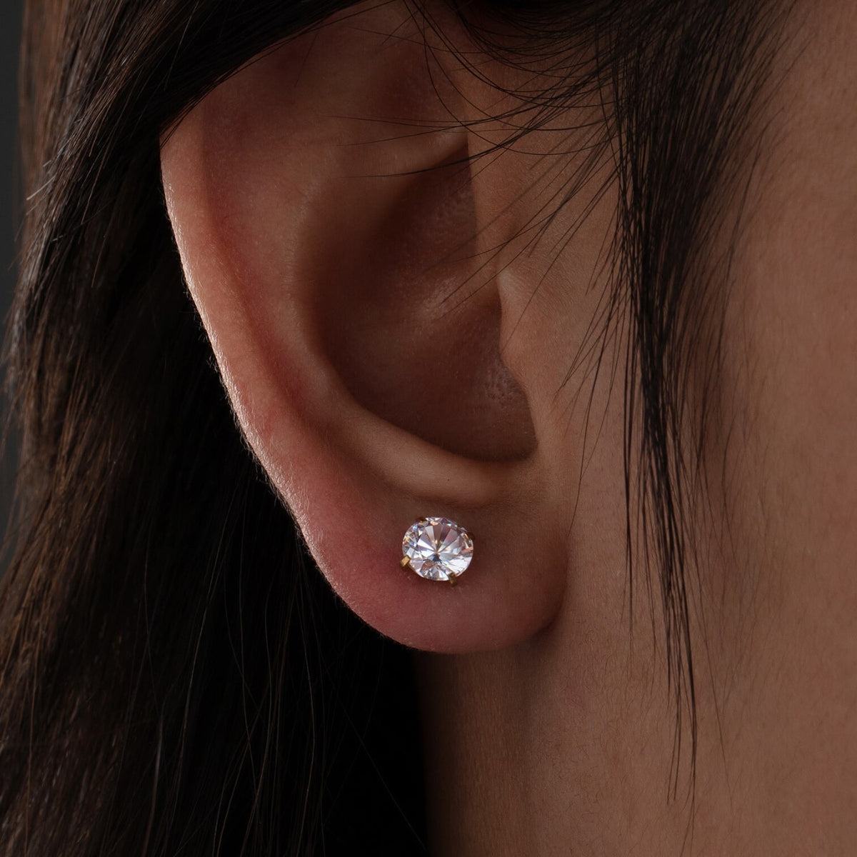 Close-up of an ear wearing a diamond earring with dark hair.