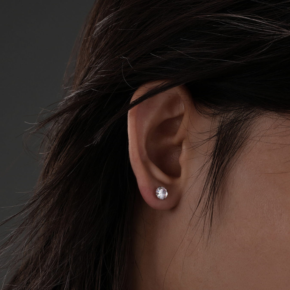 Close-up of an ear wearing a diamond earring with dark hair.