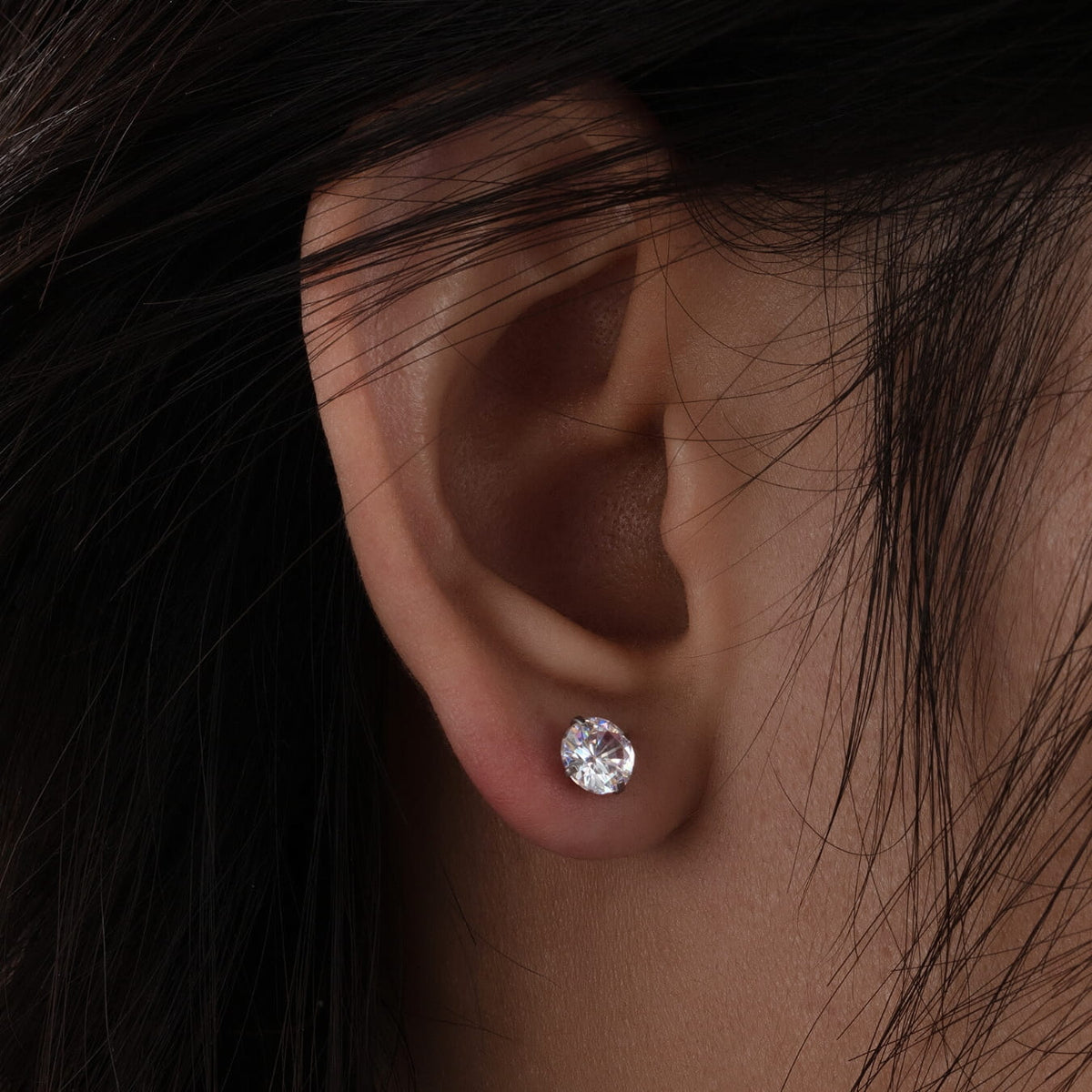 Close-up of an ear wearing a diamond stud earring with dark hair.
