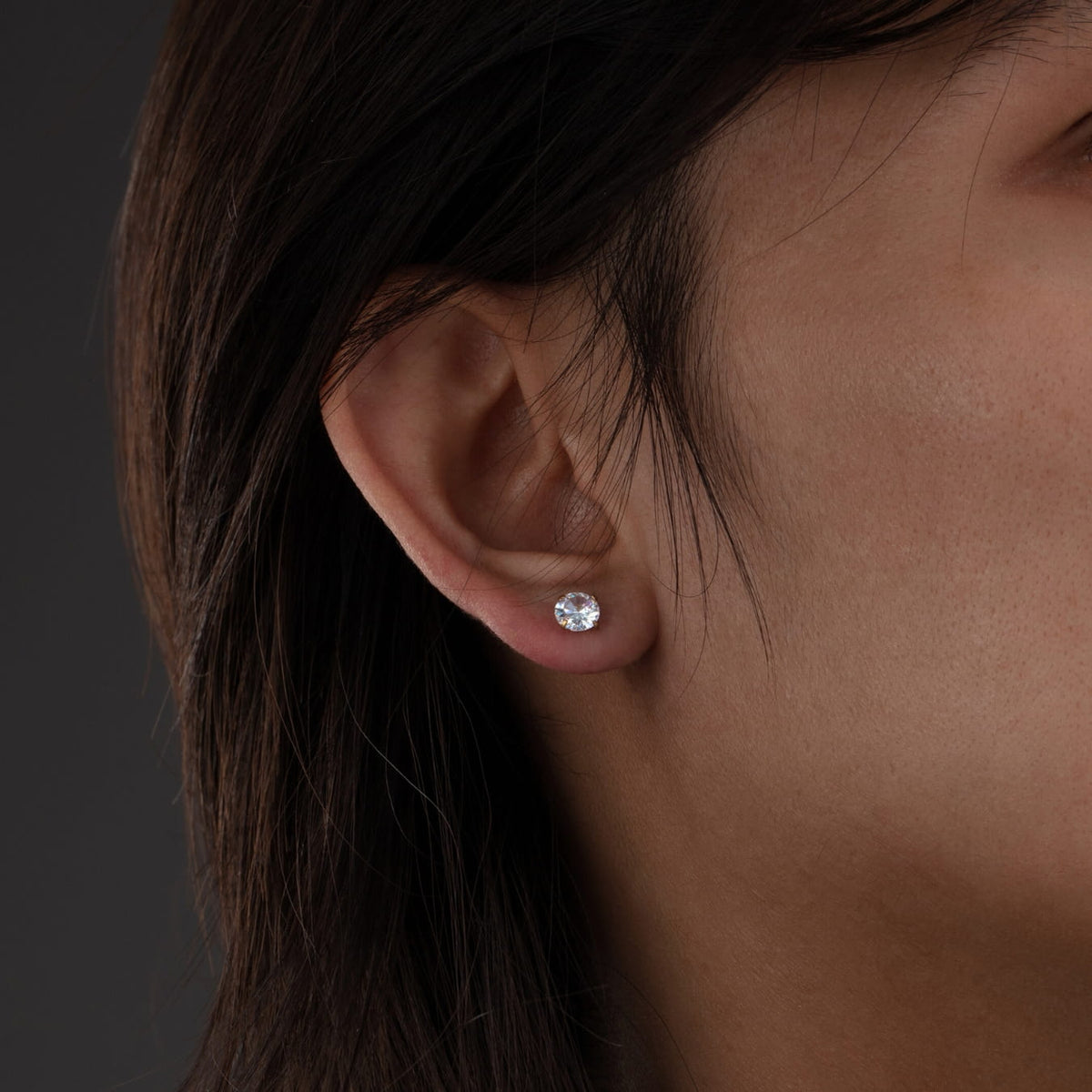Close-up of an ear wearing a diamond stud earring against a dark background