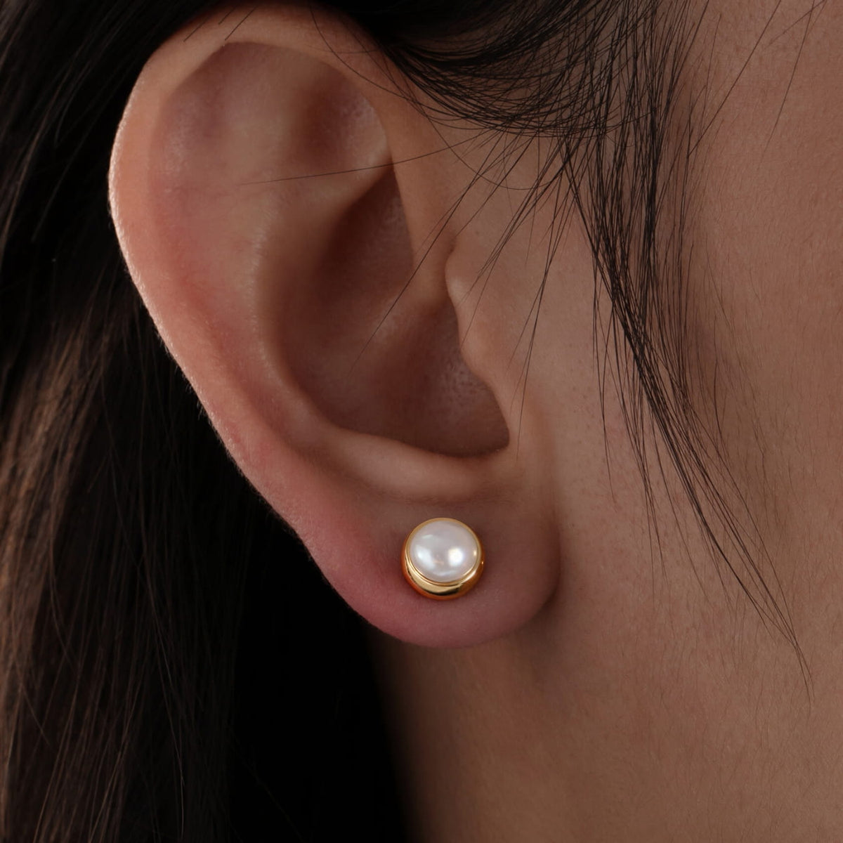 Pearl earring on a person's ear with a dark background