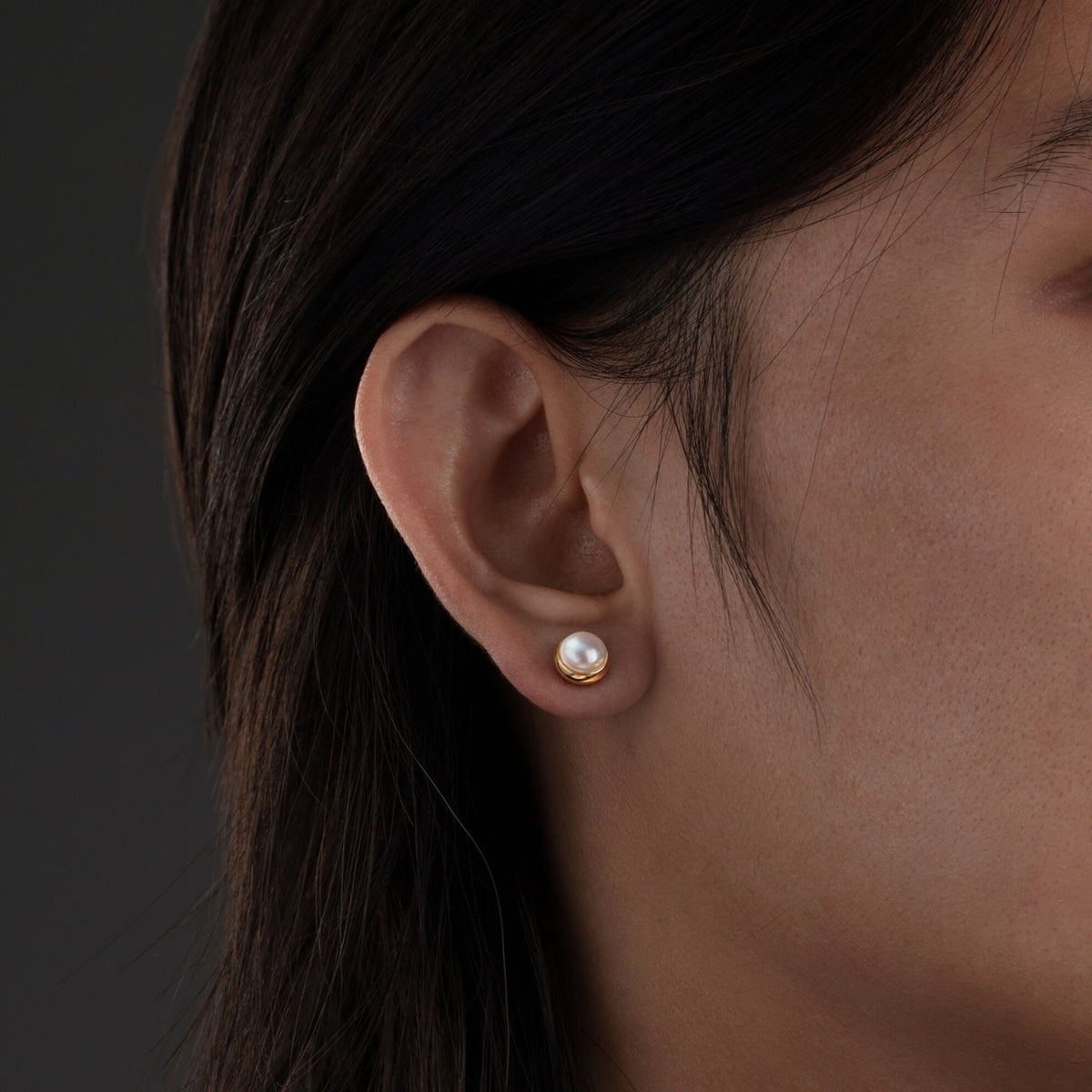 Close-up of an ear wearing a pearl earring with a dark background