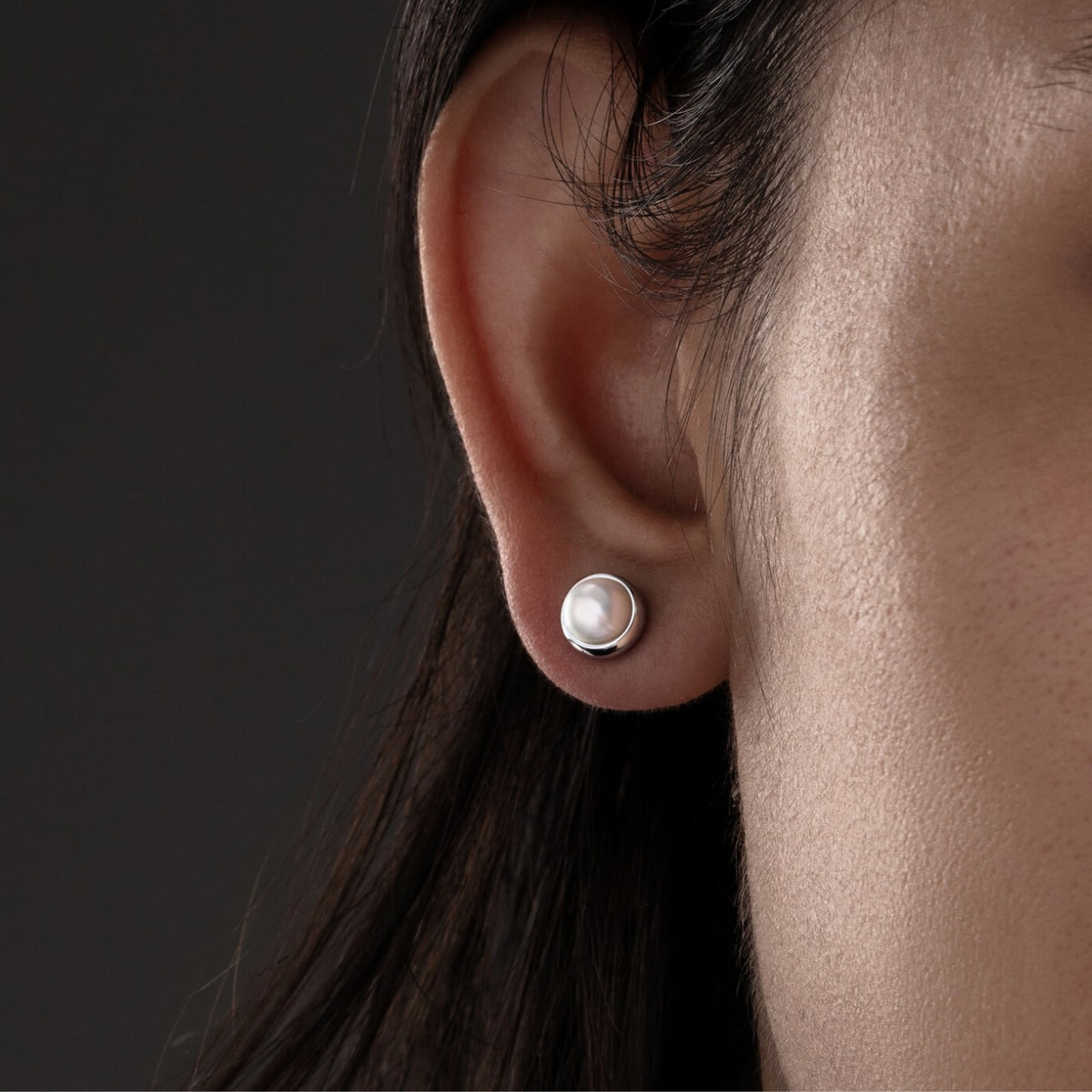 Close-up of an ear wearing a pearl earring against a dark background