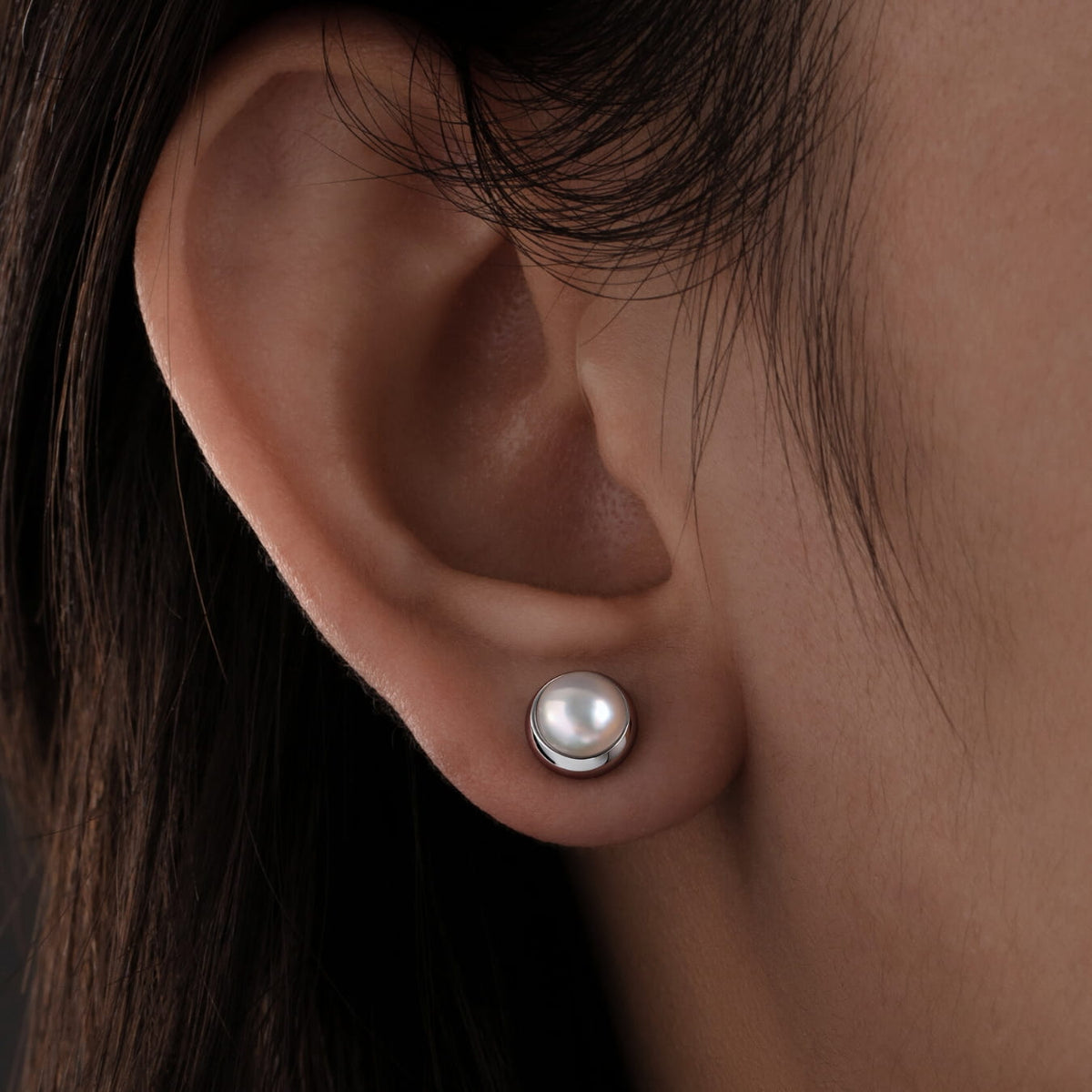 Close-up of an ear wearing a pearl stud earring with dark hair