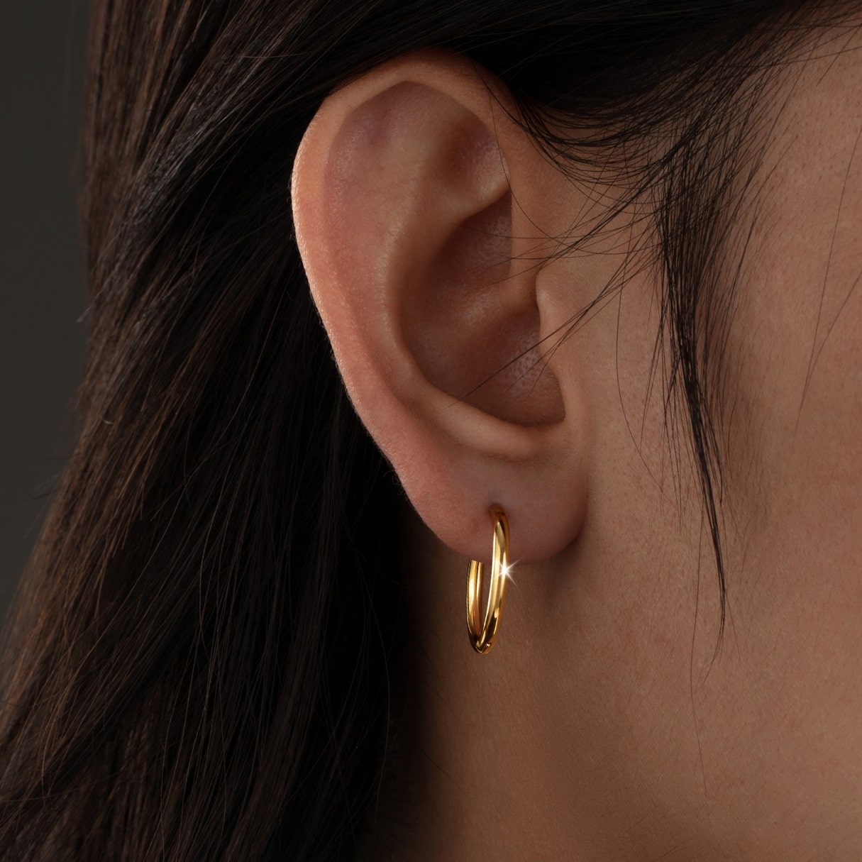 Close-up of an ear wearing a gold hoop earring with dark hair.
