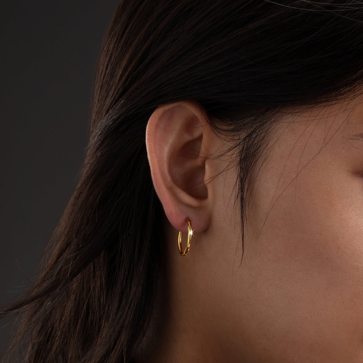 Close-up of an ear wearing a gold hoop earring with dark hair